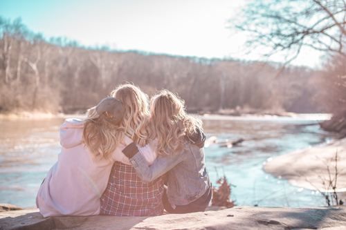 Groepje vrouwen die zitten aan een meer en elkaar omhelzen